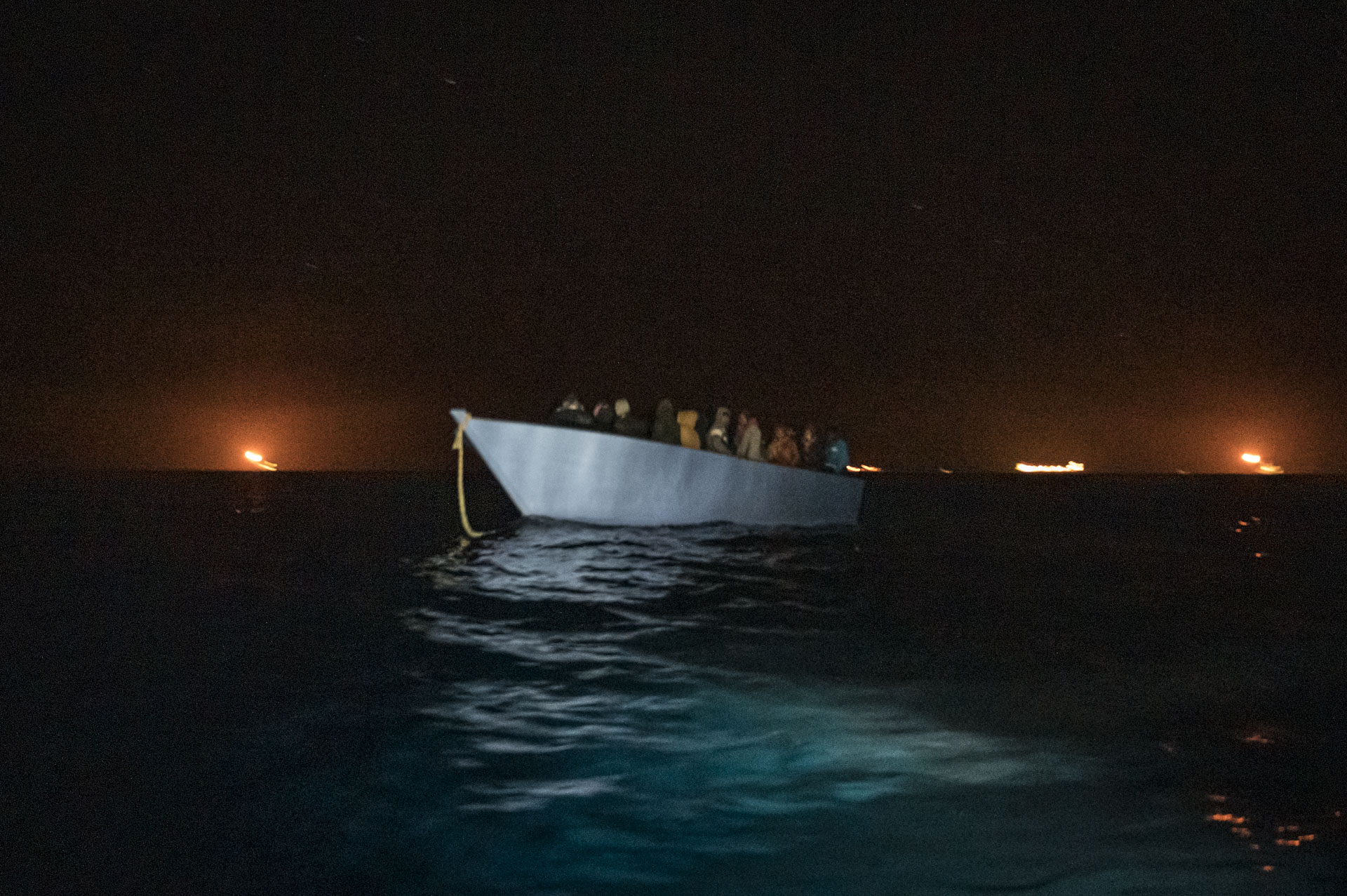 Seenotrettung – Im Schatten des Wohlstandes — Am frühen Morgen entdeckt das deutsche Rettungsschiff Sea-Watch 3 nördlich der libyschen Küste im Offshore-Feld Bahr Essalam im Mittelmeer ein Flüchtlingsboot. Zwischen den Gasfackeln der 