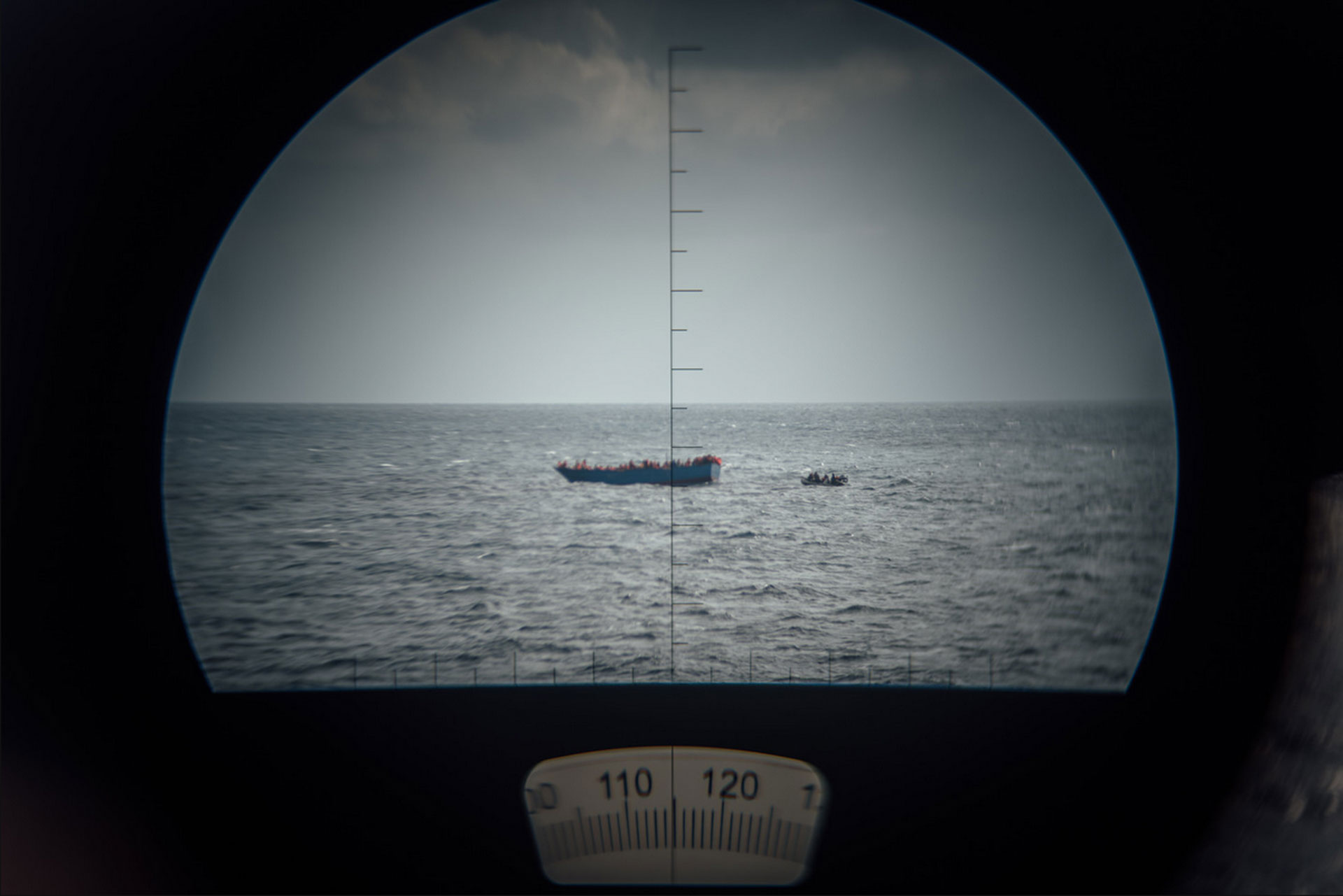 Mediterranean Rescue, Rettungseinsatz der MS Aquarius vor der Küste Libyens im stürmischen Mittelmeer. Die Rettung wird durch ein Fernglas beobachtet. Jeder 41. Flüchtling stirbt bei Überfahrt in Richtung Europa, 12.2016, Mittelmeer zwischen Italien und Libyen. © Kevin McElvaney