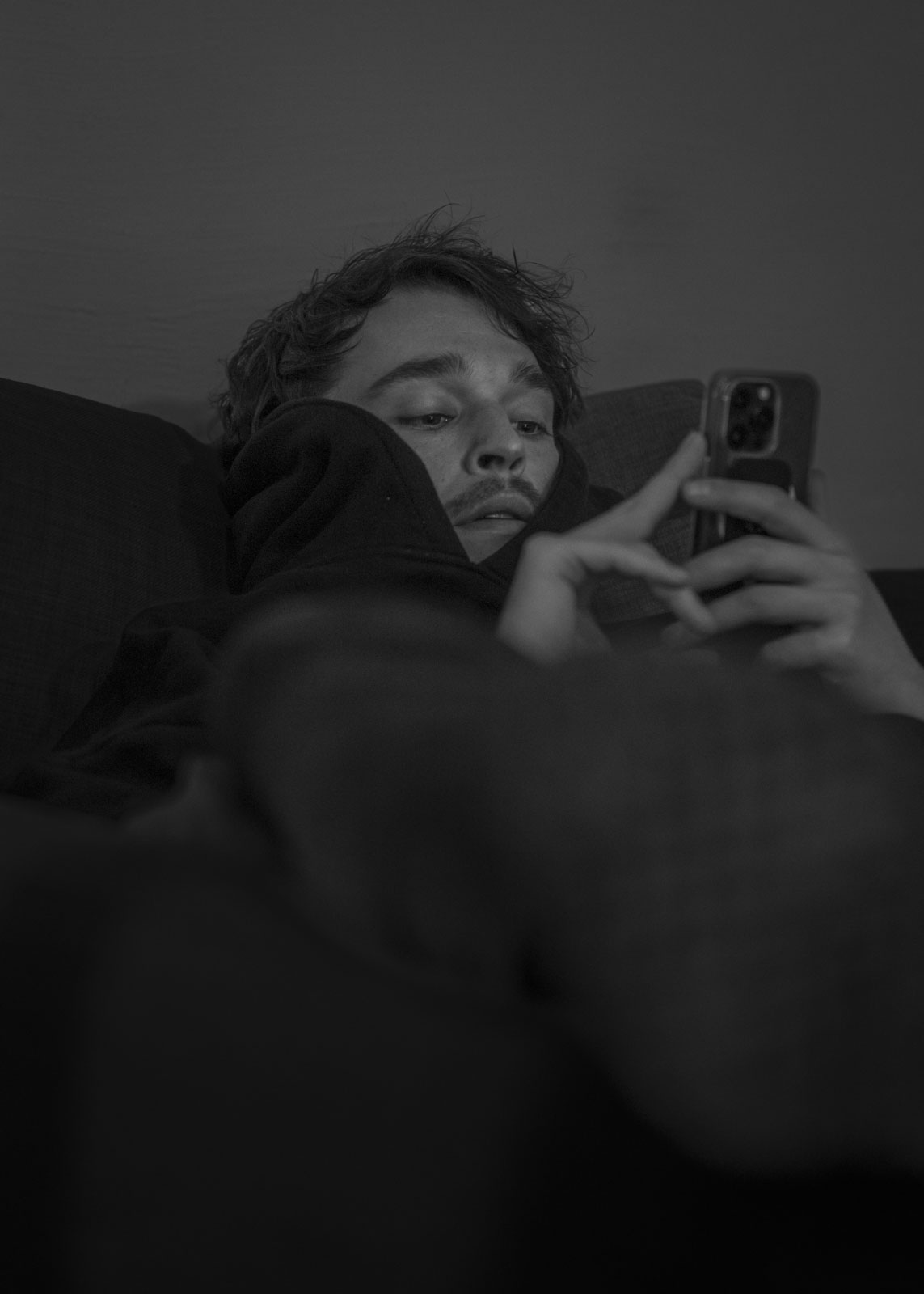 ZIAN liegend auf dem Sofa im Backstage des Kulturlokals Albani in Winterthur. Er vertreibt sich die lange Wartezeit zwischen Soundcheck und Konzertbeginn mit dem Smartphone. 18.01.2024, Winterthur, Schweiz, © 2024 Raphael Diethelm