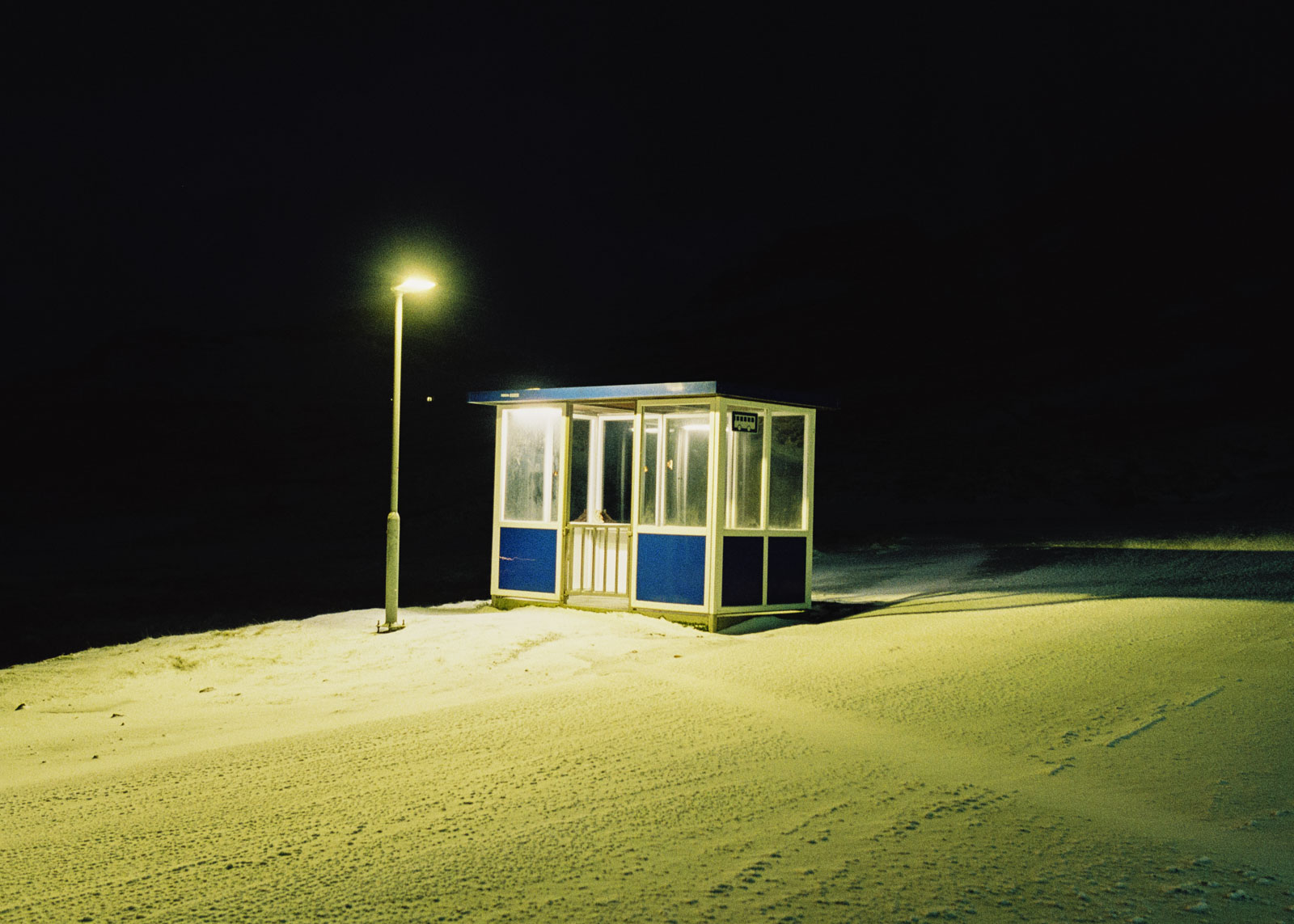 A bus stop at night next to the Effo Kollafjordur gas station. Although the Faroese have a well-developed public transport system, they cherish their own cars. A saying about their own people declares, «Why does he even need a raincoat? He has a car after all.» 14.12.2022, Kollafjordur, Faroe Island, ©2022 Niclas Tiedemann