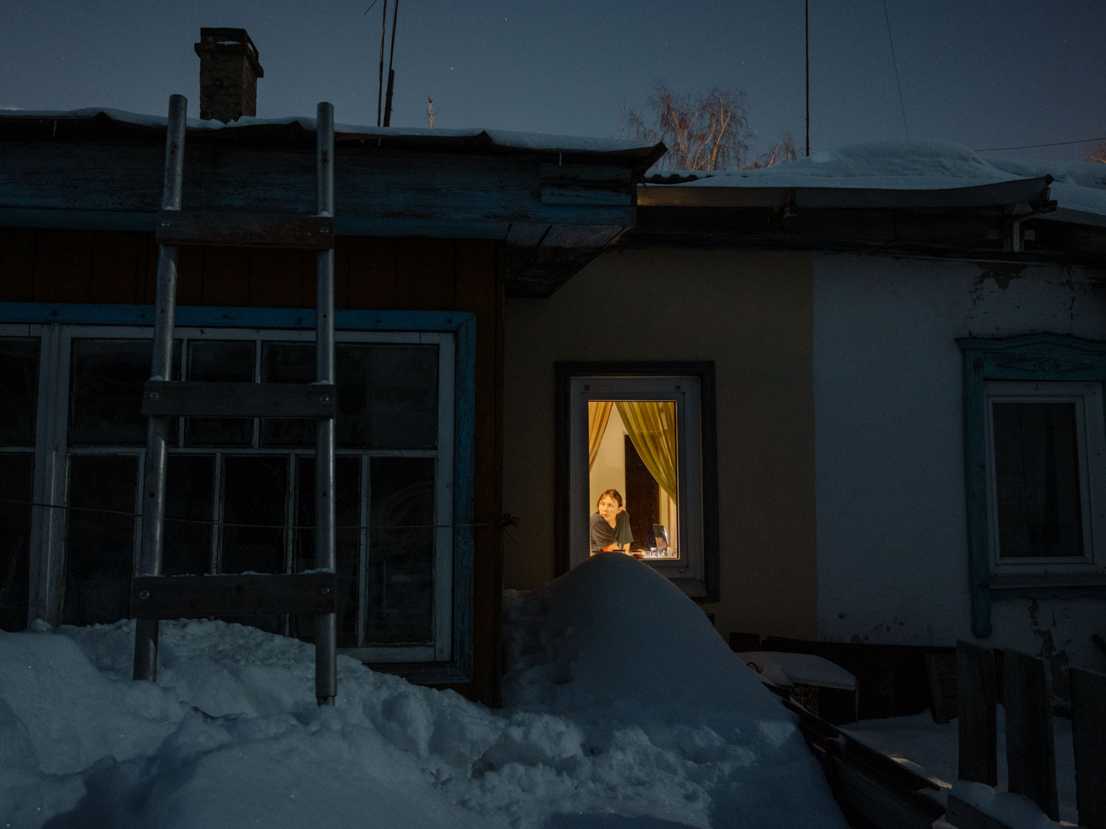 Am Ende des Winters liegt in Tomsk so viel Schnee, dass er bis zur Fensterbank reicht und die Wände zu erdrücken scheint. 05.02.22 Meine Mutter im Fenster meines Elternhauses. Tomsk, © 2022 Aliona Kardash