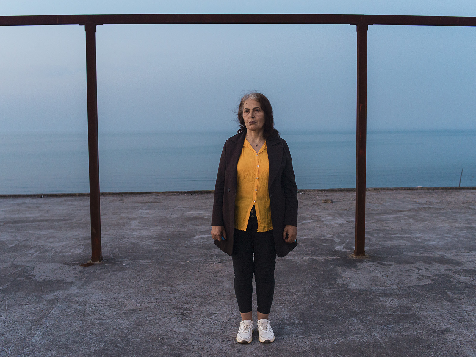 Rojan. Rojan Rajabpour (meine Mutter) neben den Bauwerken am Strand. Der unkontrollierte Bau von Freizeit- und Touristengebäuden entlang der Küste, der in den letzten Jahren ohne Beachtung der gesetzlichen Küstenschutzgrenzen durchgeführt wurde, hat erhebliche Auswirkungen auf die Zerstörung des natürlichen Ökosystems des Meers gehabt. 20.04.2024, Kelachay (Guilan Province), Iran, © 2024 Armina Ahmadinia