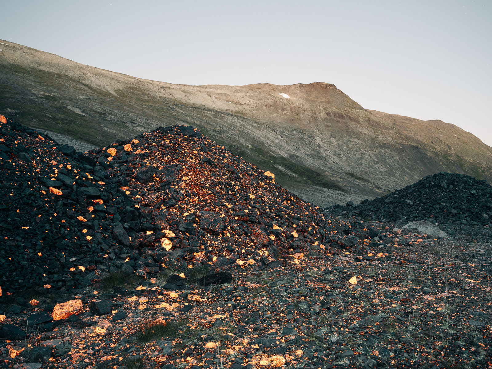 Das Kuannersuit/Kvanefjeld-Vorkommen wurde ursprünglich aufgrund seines Uran-Gehaltes erkundet. Dazu wurden über Jahrzehnte Bohrungen durchgeführt und Erkundungstunnel angelegt. Tausende Tonnen an Gestein wurden zur weiteren Untersuchung nach Dänemark gebracht, der Rest des Materials blieb in großen Haufen im Tal nahe Narsaq zurück. Nachdem die Dänen 1984 beschlossen doch nicht in die Atomkraft einzusteigen wurde das Projekt aufgegeben. Das nach Dänemark transportierte Material wird in Dänemark als Atommüll behandelt und entsprechend gelagert. 1.8.2023 Narsaq, Grönland © 2023 Jan Richard Heinicke