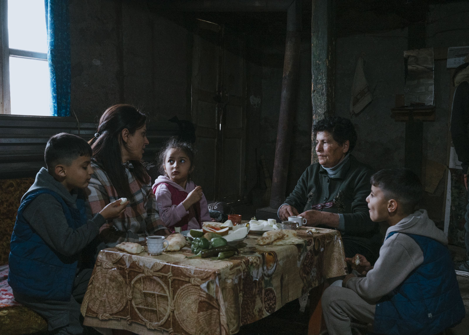 Arevik sitzt beim Abendessen mit ihren Kindern und der Frau, bei der sie derzeit untergekommen sind. Nachdem Aserbaidschan 2023 die Kontrolle über Bergkarabach übernommen hatte, mussten sie nach Armenien fliehen. Jetzt leben sie bei einer Familie in einem Dorf nahe der Grenze zu Aserbaidschan. 06.11.2024, Tegh, Armenien, © 2024 Jana Islinger