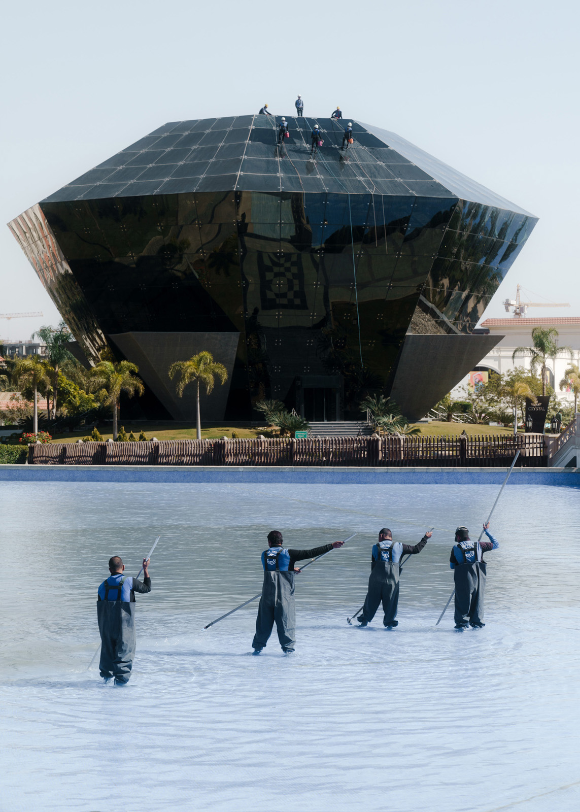 Putzkräfte reinigen den Poolbereich und die Fassade des Restaurants im ersten Hotel, das in der neuen Hauptstadt eröffnet hat. Das St. Regis Almasa, das hauptsächlich von einigen hochrangigen Militärs und Regierungsbeamten, aber auch einigen wohlhabenden Ägyptern und Touristen besucht wird, muss von einer wesentlich höheren Anzahl Angestellter in Stand gehalten werden., 03.02.20234, New Administrative Capital, Ägypten, © 20234 Louis Roth