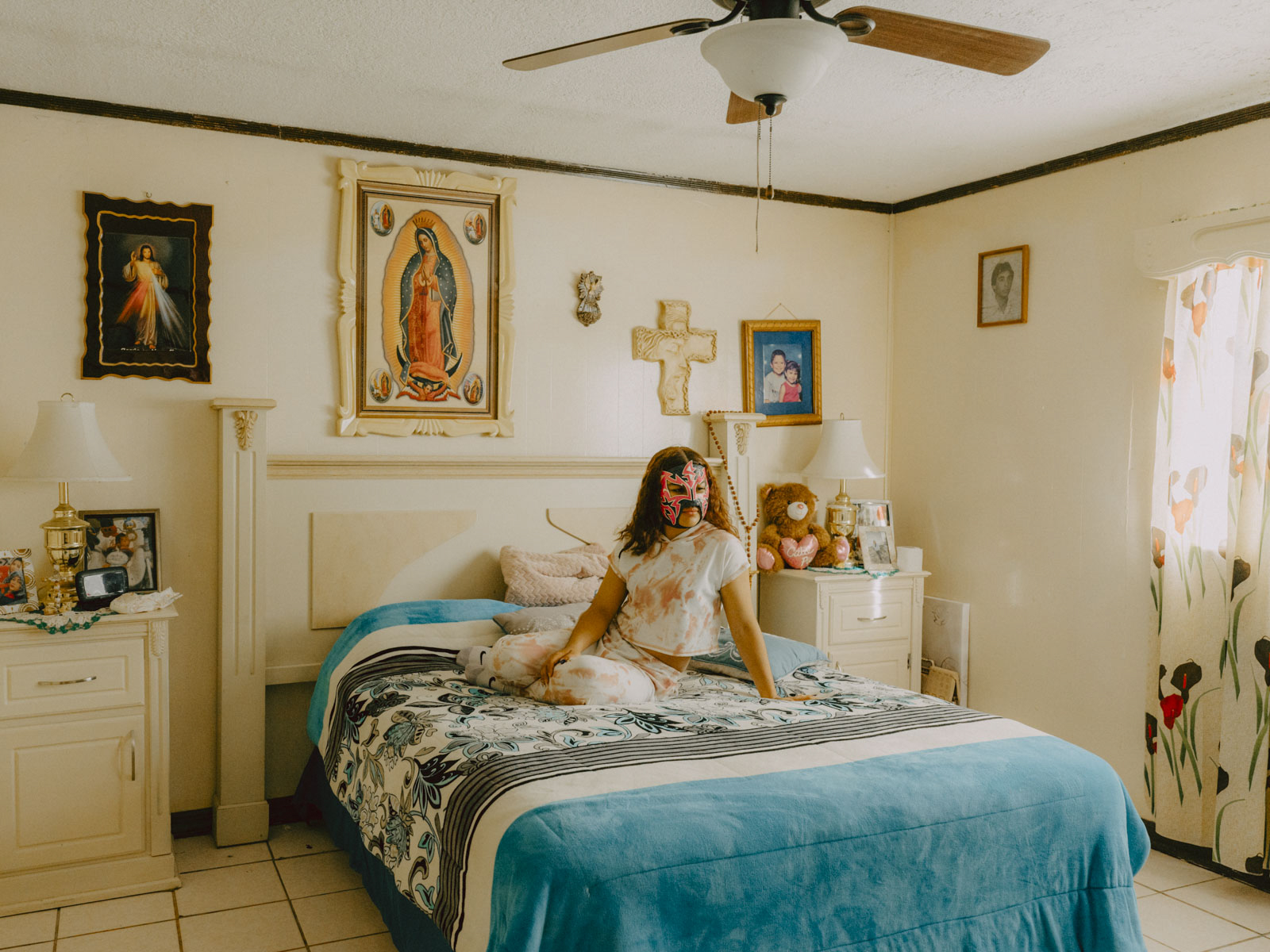 Sayuri sitzt auf dem Bett ihrer Großmutter in Ciudad Juárez, Mexiko. Mit 15 Jahren ist sie die jüngste Profi-Wrestlerin der Stadt. Die Maske erlaubt ihr ein Doppelleben; ihre Mitschüler wissen nicht, dass sie an den Wochenenden vor Tausenden von Zuschauern kämpft. 14.03.2023, Ciudad Juárez, Mexiko, © 2023 Jana Margarete Schuler