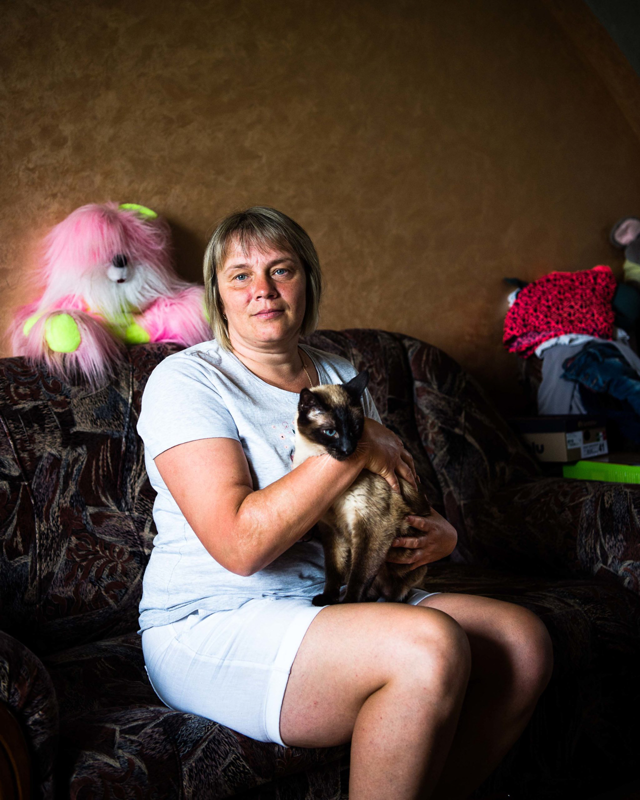 Inna S. posiert auf ihrem Sofa mit einer Katze für ein Porträt. Sie und ihr Mann nehmen auf ihrem Grundstück neben verletzten und behinderten Vögeln auch 10 Hunde, 9 Katzen, Chinchillas und Fische auf. Aufgenommen am 21. Juni 2021 in der Nähe von Khmelnytskyi im Westen der Ukraine, © 2021 Finn Winkler