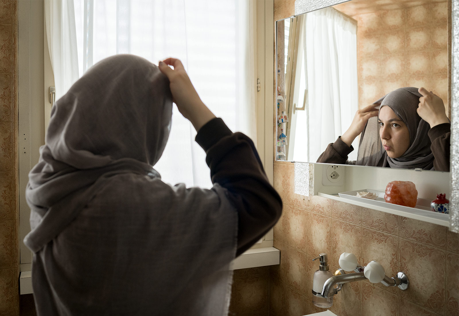 Feyza Hilal Karabulut lädt mich in ihr Zuhause ein. Sie zeigt mir das Anlegen ihres Hijabs, eine ruhige, alltägliche Geste des Ankommens im Tag. Diese Szene stellt sie für mich nach. 11.09.2025, Basel-Landschaft, Schweiz, © 2025 Azura Silberschmidt
