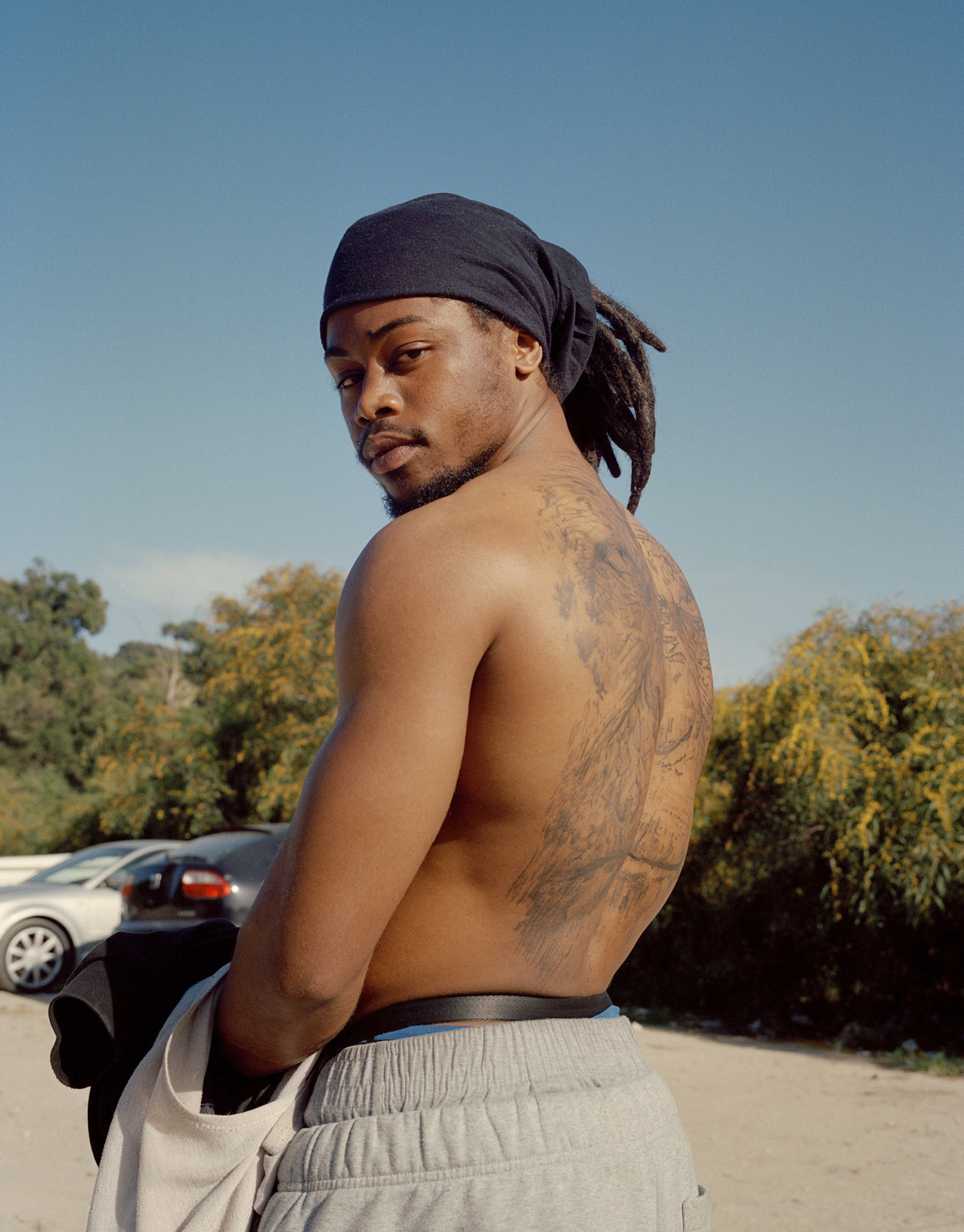 «G», ein Mitglied des Rap-Kollektivs GTO Fam, in Segundo Torrão. Durch Musik artikulieren lokale Künstler Erfahrungen von Verdrängung und Marginalisierung im Kontext der städtischen Transformation Lissabons. Hier zeigt er sein «Planet der Affen»-Rückentattoo. Segundo Torrão, Trafaria, Portugal. ©2023 Jessica Dreier