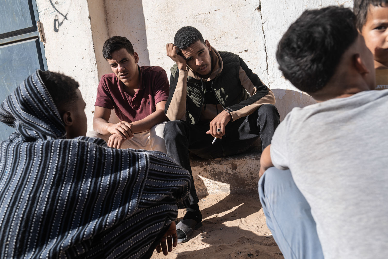 Vor 50 Jahren drang die Kolonialmacht Marokko in die Westsahara ein. Tausende Sahrauis flohen in die lebensfeindliche Hamada-Wüste, wo sie seit dem in Flüchtlingslagern ausharren, Junge Männer sitzen vor einem Friseursalon in den Flüchtlingslager der Sahrauis, 29.11.2025, Refugee Camp Aussert, Algerien, © 2025 Niklas Thalmann